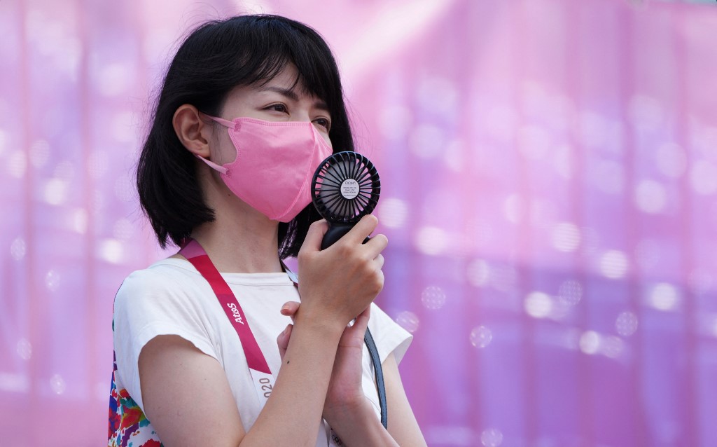 Jornalista japonesa acompanha jogo de basquete 3x3, ao ar livre, com ventilador portátil: recomendação das autoridades para que população evite fazer exercícios ao ar livre devido às altas temperaturas e à unidade (Foto: Vladimir Astapkovich / Sputnik / AFP)