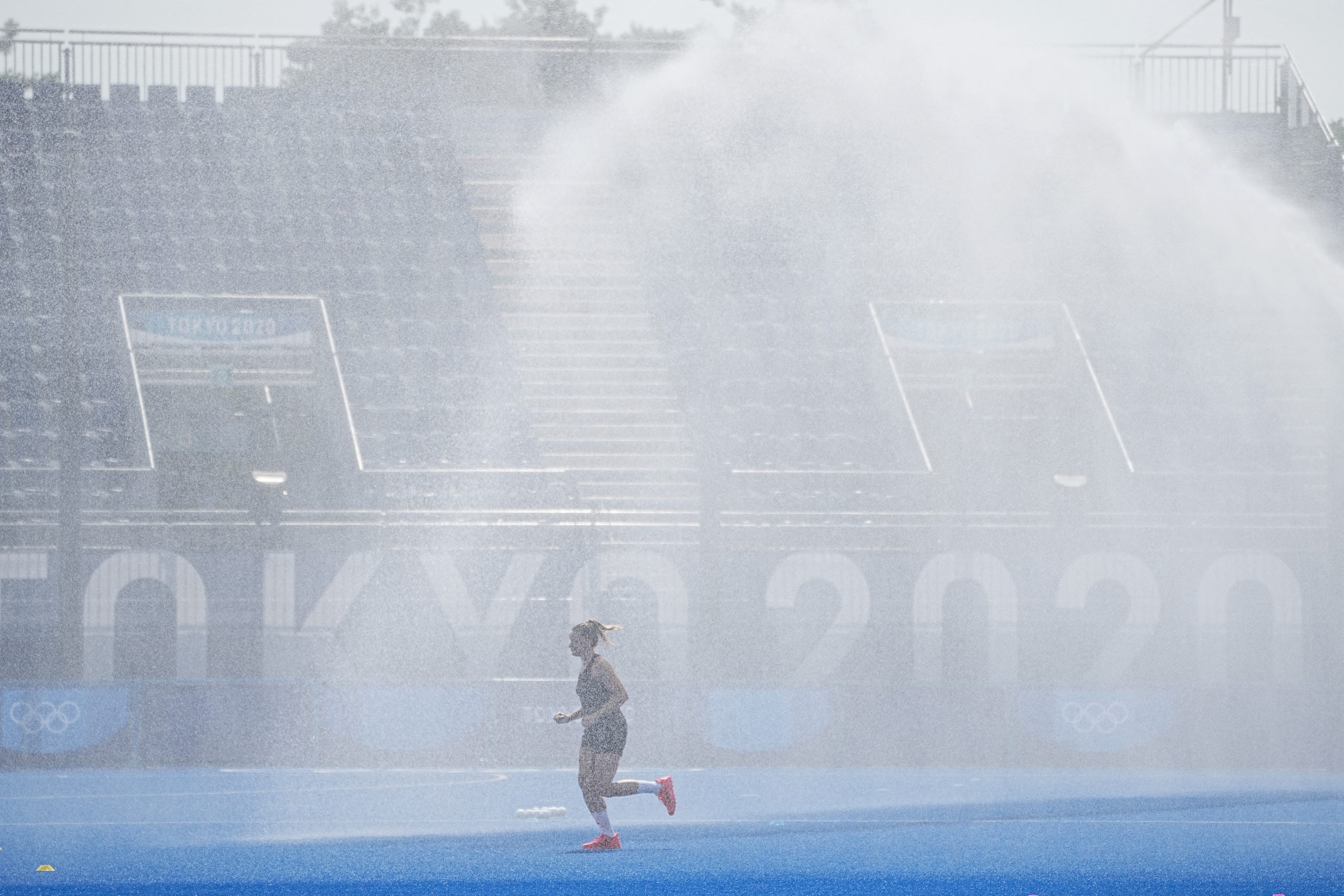 Jogadora de hóquei da Alemanha corre em meio a água do sistema de irrigação: equipamentos usados para refrescar, além do gramado, atletas (Foto: Michael Kappeler/ DPA / AFP -20/07/2021)