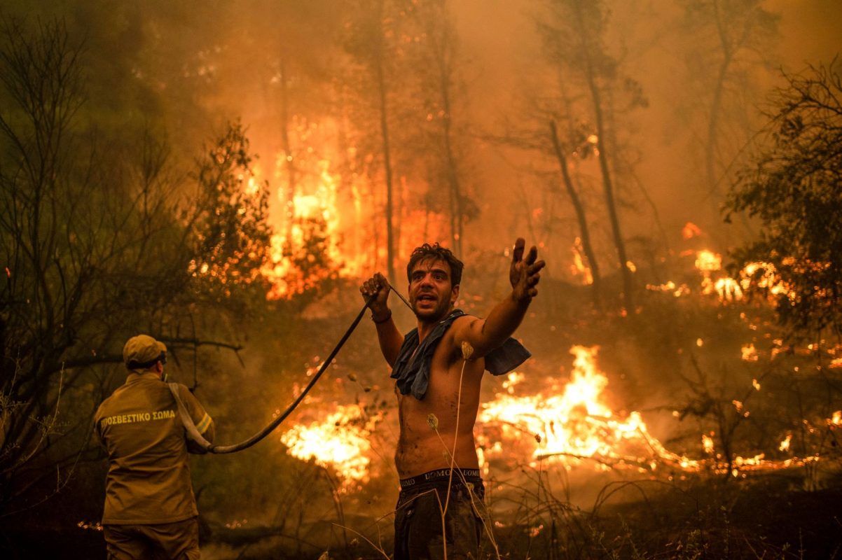 Morador ajuda bombeiro no combate ao incêndio na ilha grega de Eubeia, que arde desde o primeiro dia de agosto: países ricos não cumprem promessas de financiamento climático (Foto: Angelos Tzortzinis / AFP)
