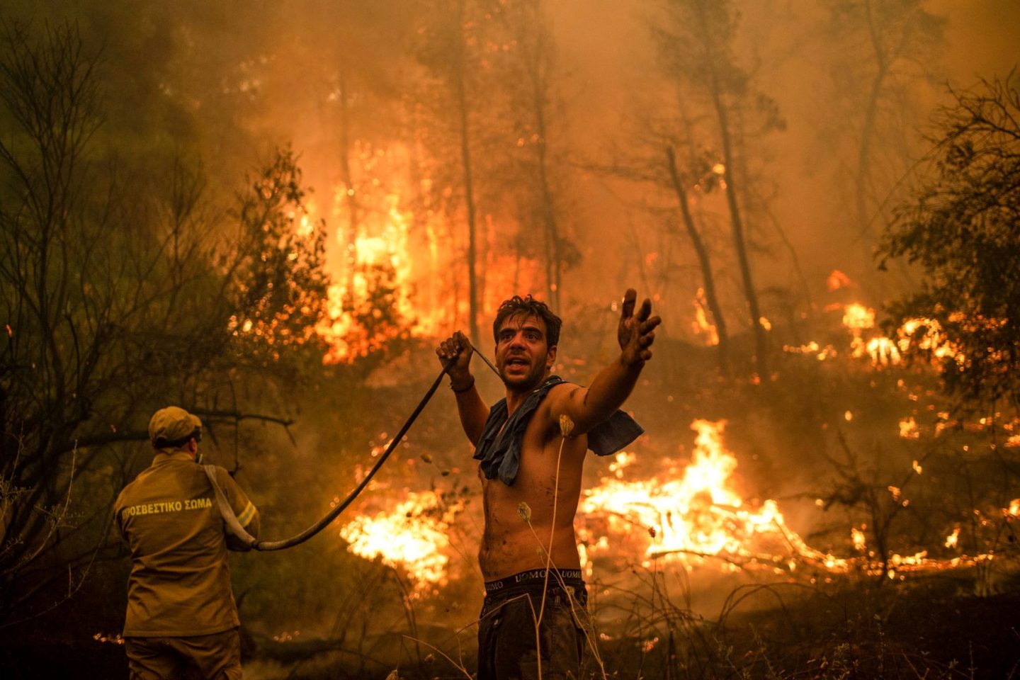 Morador ajuda bombeiro no combate ao incêndio na ilha grega de Eubeia, que arde desde o primeiro dia de agosto: países ricos não cumprem promessas de financiamento climático (Foto: Angelos Tzortzinis / AFP)