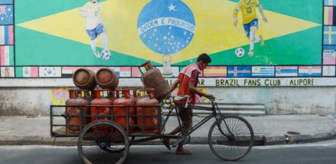 Um trabalhador carrega cilindros de gás em frente a uma arte da bandeira do Brasil desenhada em uma parede em Calcutá, na Índia. Foto Debarchan Chatteriee/NurPhoto, via AFP. Junho/2021