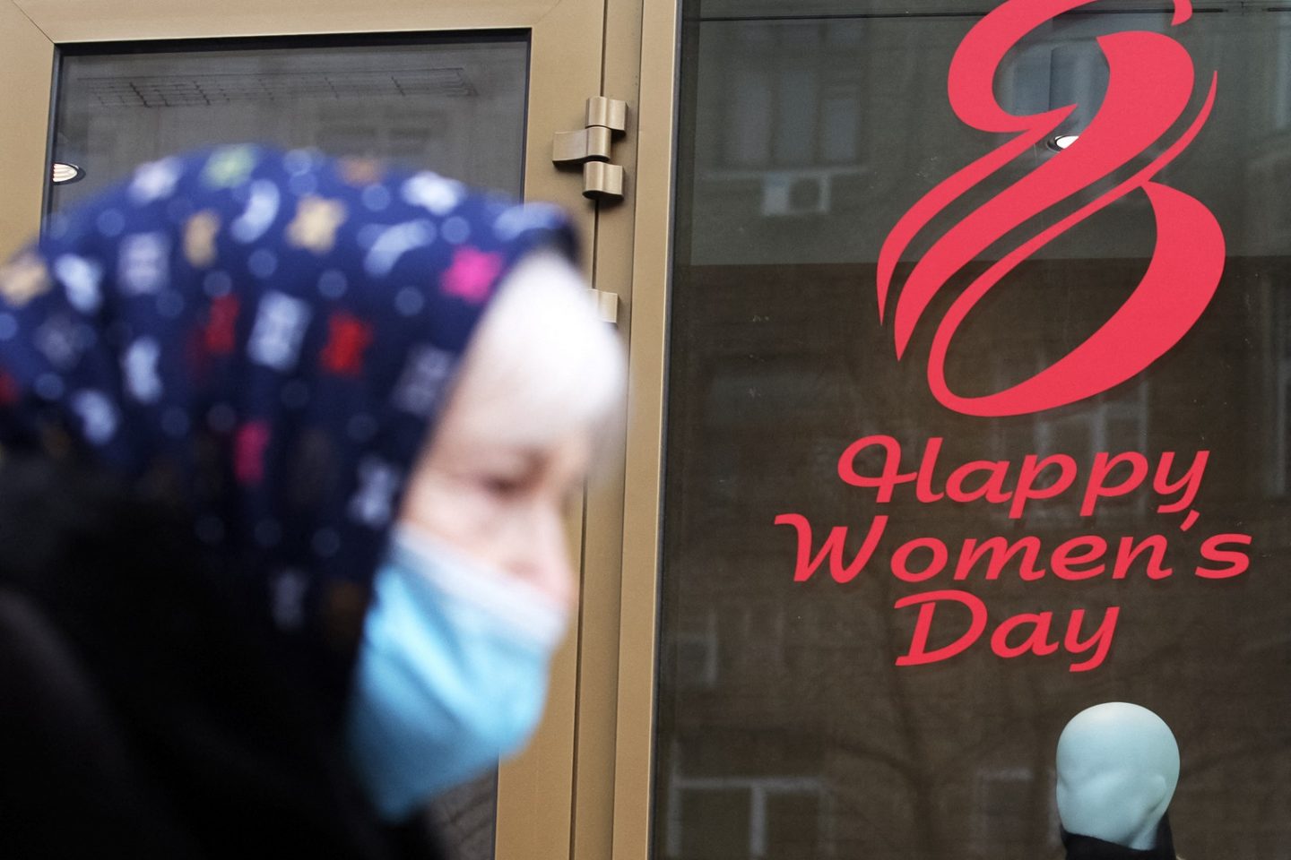 Em Kiev, na Ucrânia, mulher passa com máscara de proteção contra a covid-19 diante de um cartaz em comemoração ao Dia Internacional da Mulher. Foto STR/NurPhoto/AFP