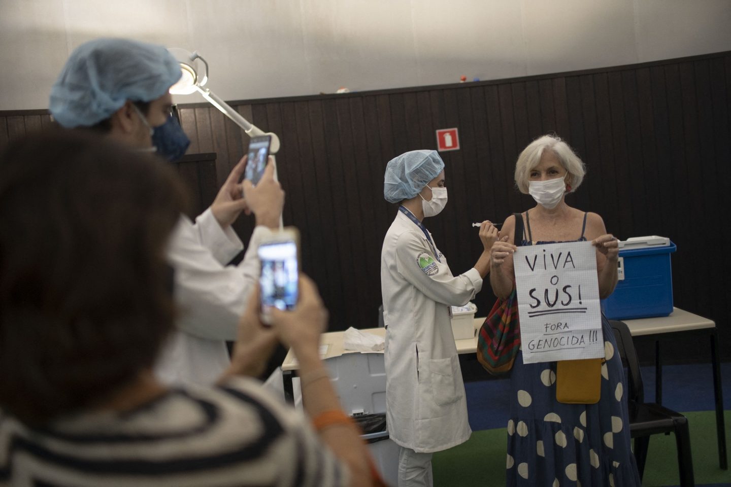 Ao ser vacinada no Planetário, no Rio de Janeiro, mulher segura um cartaz celebrando o trabalho do SUS e criticando o presidente Jair Bolsonaro. Foto Mauro Pimentel/Março/2021