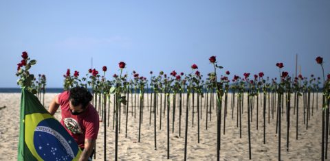 Manifestante segura bandeira brasileira ao lado de rosas colocadas pela ONG Rio de Paz na praia de Copacabana, no Rio de Janeiro, em memória ao Brasil de meio milhão de vítimas da covid-19. Foto Carl de Souza/AFP. Junho/2021