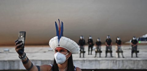 Brasil, América do Sul: mulher indígena, usando máscara contra a covid-19, tira selfie em frente à tropa de choque no prédio do Supremo Tribunal Federal, em Brasília. Foto Carl de Souza/AFP. Agosto/2021