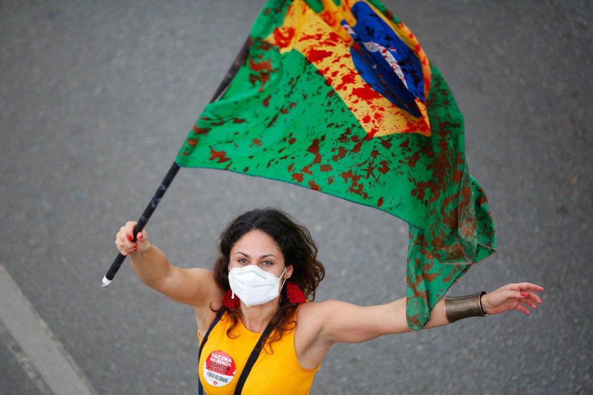 Em Brasília, segurando uma bandeira manchada de vermelho, manifestante protesta contra o descaso do governo e lembra as quase 600 mil vidas perdidas para covid-19 no Brasil. Foto Sérgio Lima/AFP