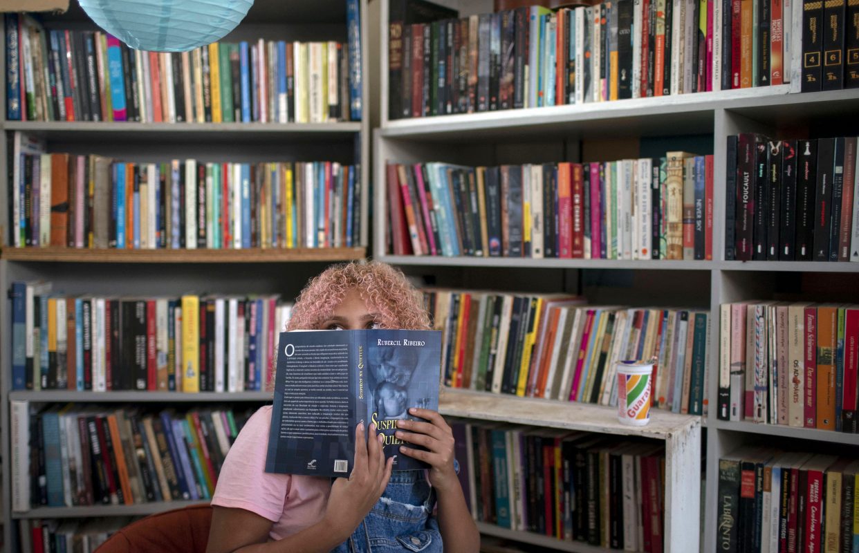 A jovem Lua Oliveira, de 12 anos, espia por trás de um livro na biblioteca pública Mundo da Lua, fundada por ela na favela dos Tabajaras, no Rio de Janeiro. Um bom exemplo de resistência. Foto Mauro Pimentel/AFP