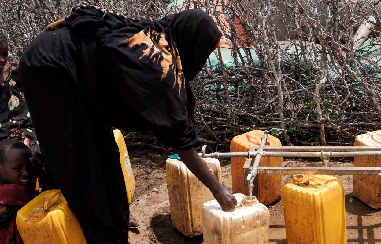 Ao lado dos filhos, refugiada climática enche recipiente plástico em campo para retirantes da seca em Baidoa, na Somália: seca extrema provocou mais 43 mil mortes no país africano em 2022 (Foto: Guy Peterson / AFP - 11/09/2022)