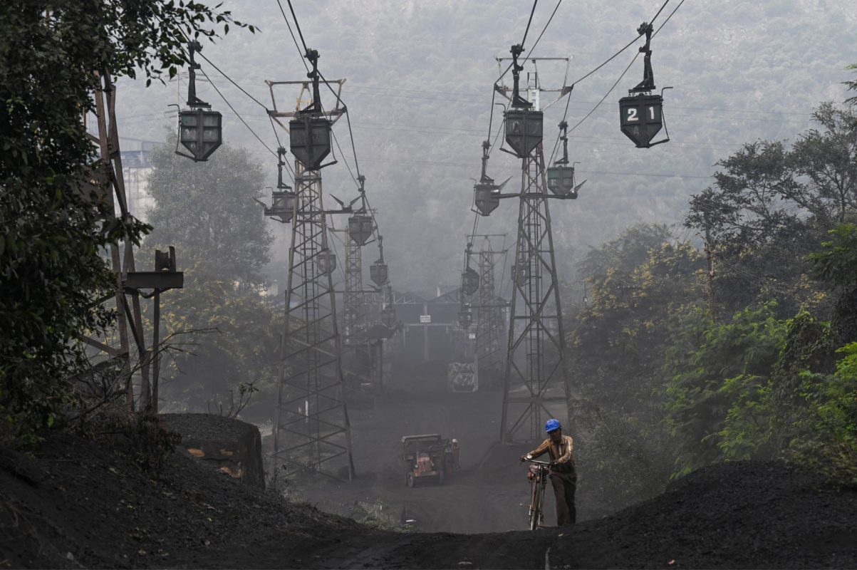 Um trabalhador empurra sua bicicleta sob uma linha de carrinhos de transporte de carvão em Sonbhadra, Uttar Pradesh, na Índia. O país tem uma das maiores pegadas ambientais do planeta. Foto Money SHARMA /AFP