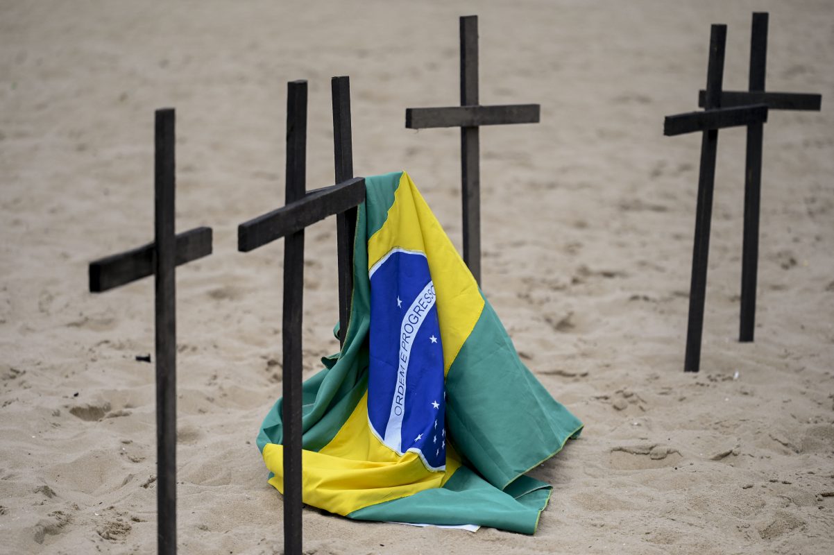 Uma bandeira brasileira é vista ao lado de uma cruz enquanto ativistas da ONG Rio de Paz e parentes prestam homenagem a Marcio Antonio, que foi a cara do luto do Covid-19 no Brasil e morreu aos 58 anos, no final de 2022. Foto Mauro Pimentel/AFP