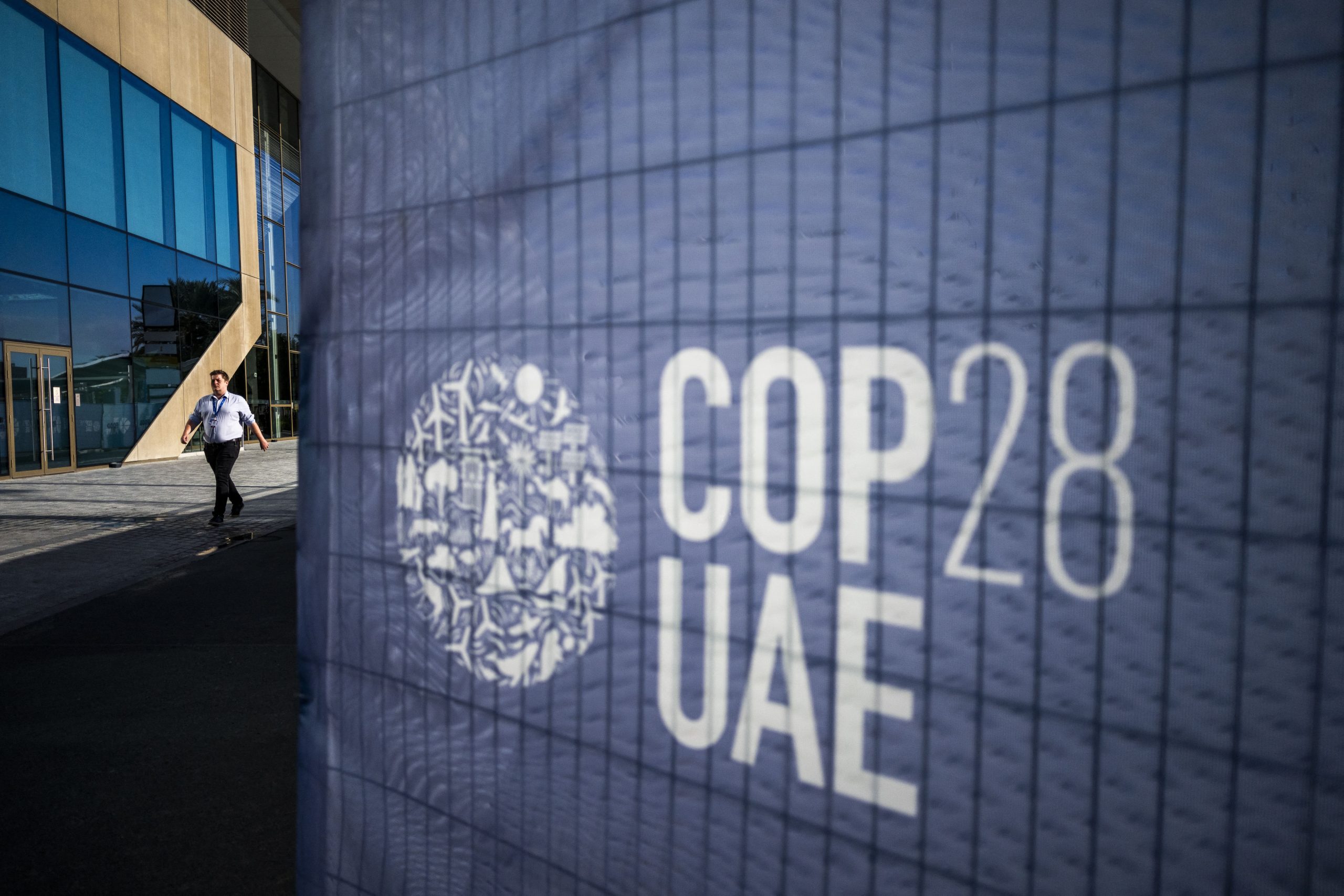 Homem passa por uma placa da COP28, em Dubai, onde se realiza a Conferência Climática. Cresce a pressão para que os países tomem medidas mais efetivas para combater a crise climática. Foto Jewel Samad/AFP