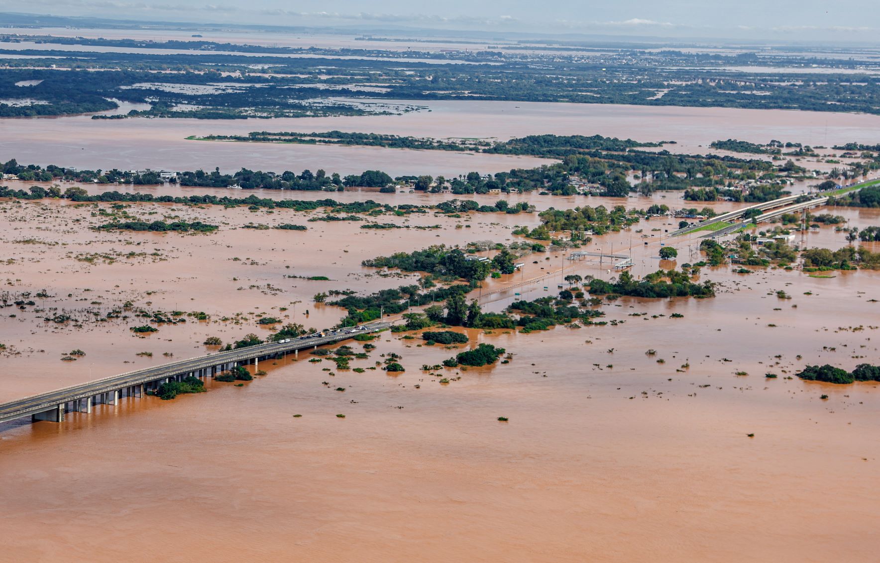 Foto coloria de área de Porto Alegre e da vizinha Canoas debaixo d'água. Na imagem é possível ver o pedaço de uma ponte no canto esquerdo, no canto inferior e em diversas partes a água está sobre os campos e apenas algumas árvores aparecem ainda não inundadas.