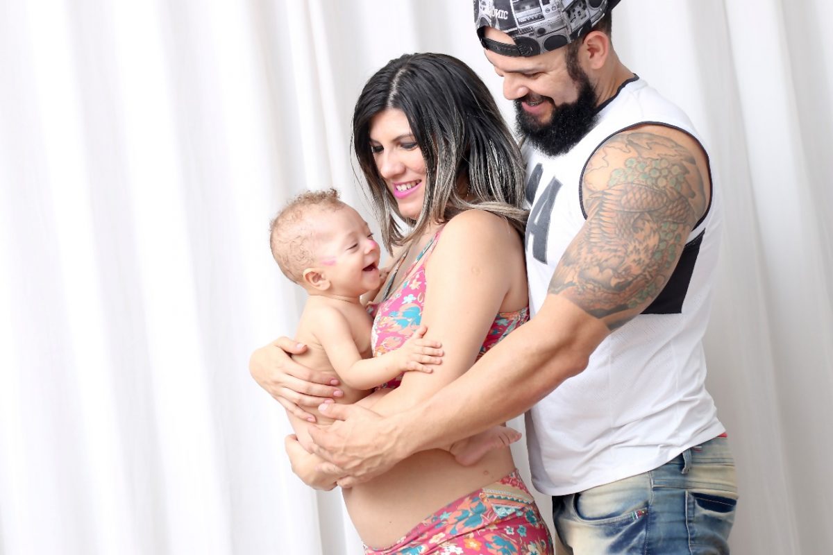 Foto colorida de Thais Emilia, o marido Beto abraçados e com Jacob no colo de Thais