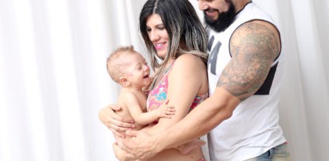 Foto colorida de Thais Emilia, o marido Beto abraçados e com Jacob no colo de Thais