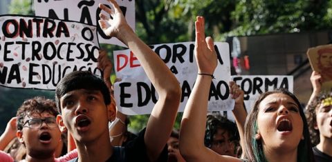 Foto colorida de estudantes em manifestação pela revogação do novo ensino médio. Na foto, jovens aparecem com cartazes e os braços levantados, enquanto gritam