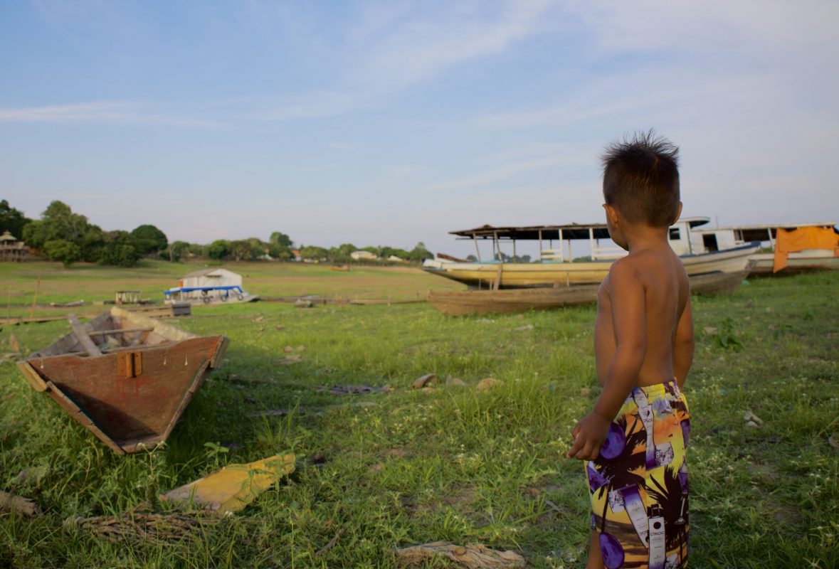 Menino observa barcos encalhados no leito seco de rio na Amazônia: crise climática afeta crianças em todas as regiões do país (Foto: Klysna Anayal -Instagram: @klysnaanayal)