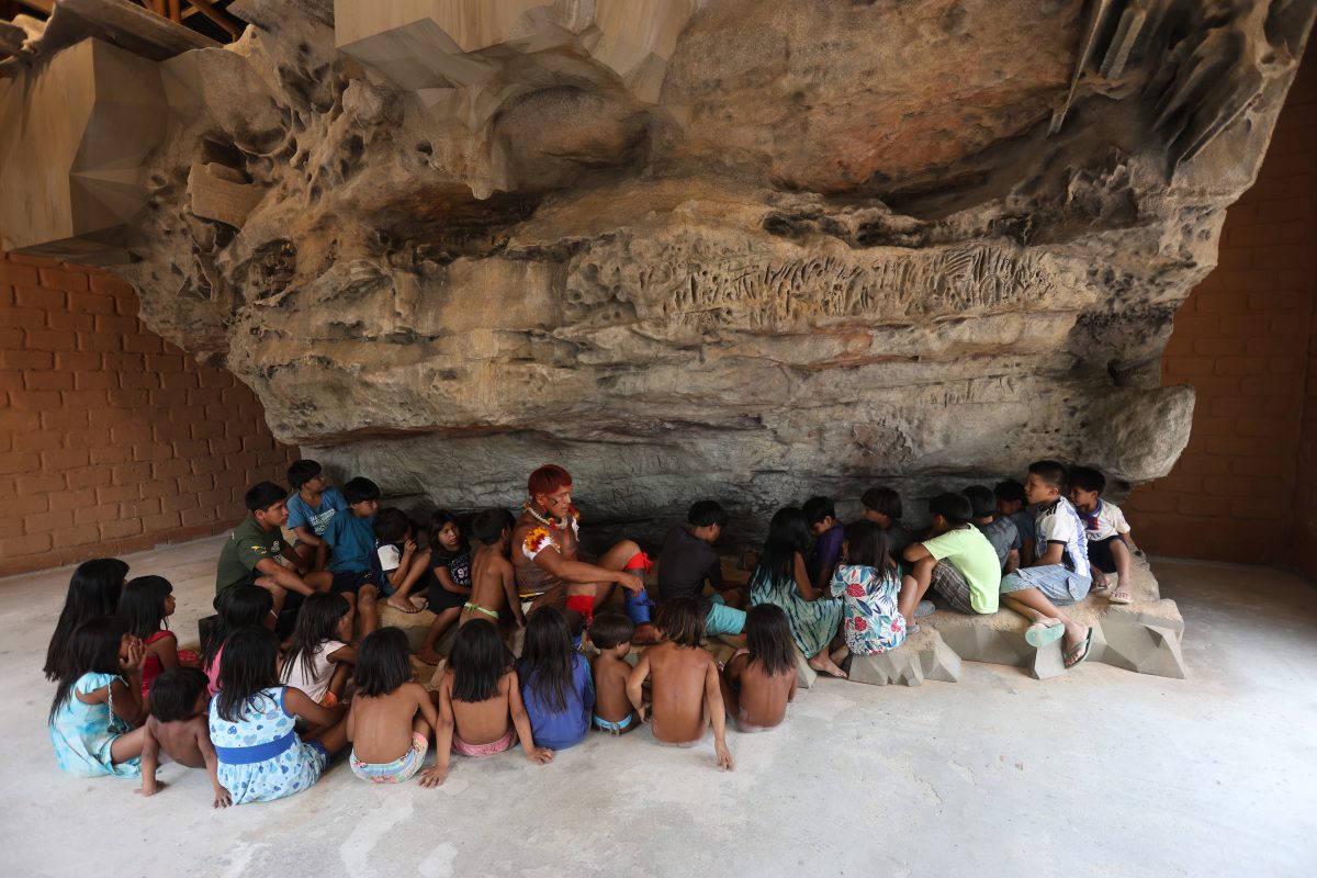 Crianças aprendendo sobre a história do guerreiro Kamukuwaká com a réplica da gruta em 3D instalada no Centro Cultural e de Monitoramento Territorial da aldeia Ulupuwene. (Alaor Filho/ Fotos Públicas)