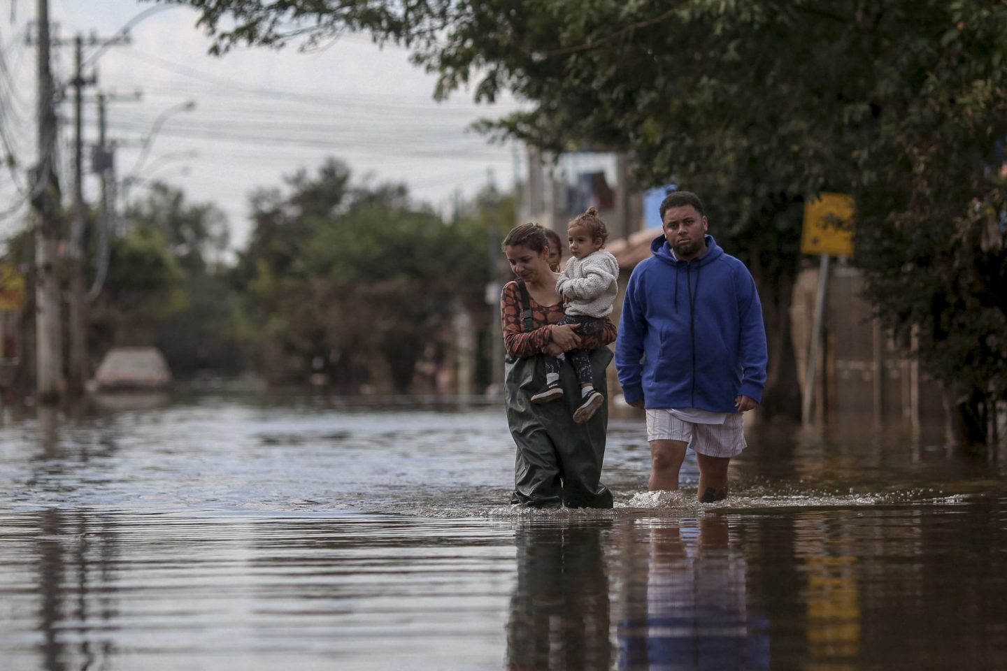 Foto colorida de mulher com criança no colo andando por rua alagada em Porto Alegre. Ao lado delas, aparece um homem também andando em meio às águas. Desastre mostram relação entre saúde materna e mudanças climáticas