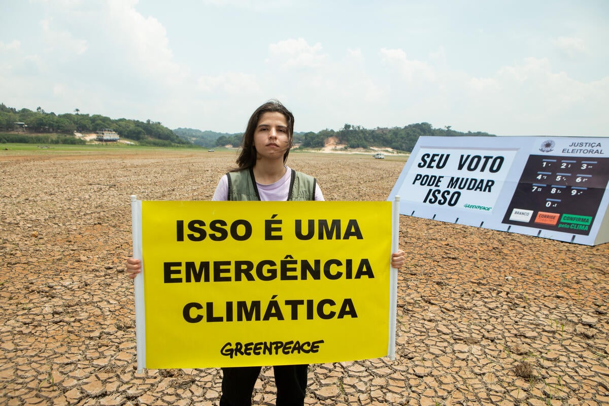 Ativista do Greenpeace com réplica gigante da urna eletrônica em lago seco em Manaus: emergência climática deve pautar ações no município e no estado (Foto: Nilmar Lage / Greenpeace)