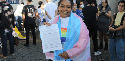 Ivoni com a bandeira trans e o documento de retificação de registro civil de Demétrio: dedicação ao acolhimento da população LGNTQIA+ após a morte do filho (Foto: DPRJ)