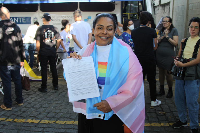 Ivoni com a bandeira trans e o documento de retificação de registro civil de Demétrio: dedicação ao acolhimento da população LGNTQIA+ após a morte do filho (Foto: DPRJ)