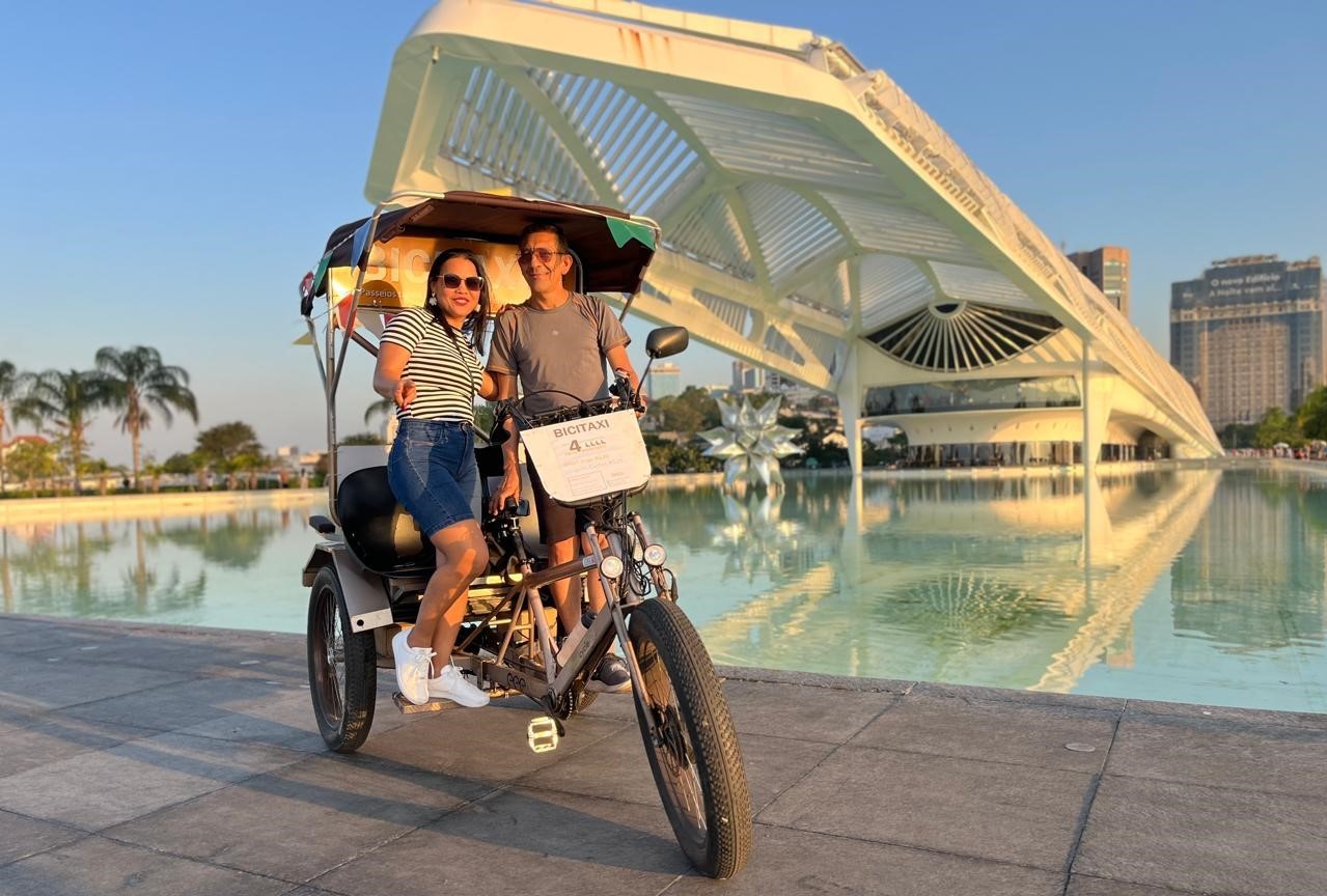 Passageiros de bicitáxi posam em frente ao Museu do Amanhã: frota de triciclos elétricos para turistas atraídos pelo transporte sustentável (Foto: Divulgação)