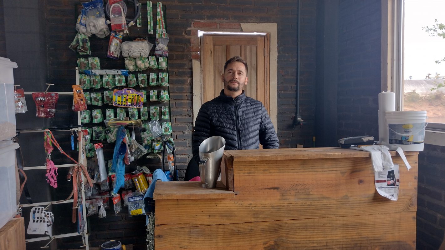 Foto colorida de Evandro Marín. Ele é um homem branco com barba e cabelo escuro. Ele usa um casaco e ao seu lado aparecem produtos da sua agropecuária