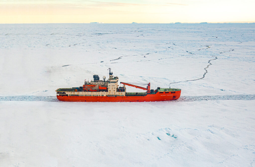 Foto colorida de navio russo utilizado na viagem à Antártica. Na imagem, o navio branco e vermelho aparece navegando no continente