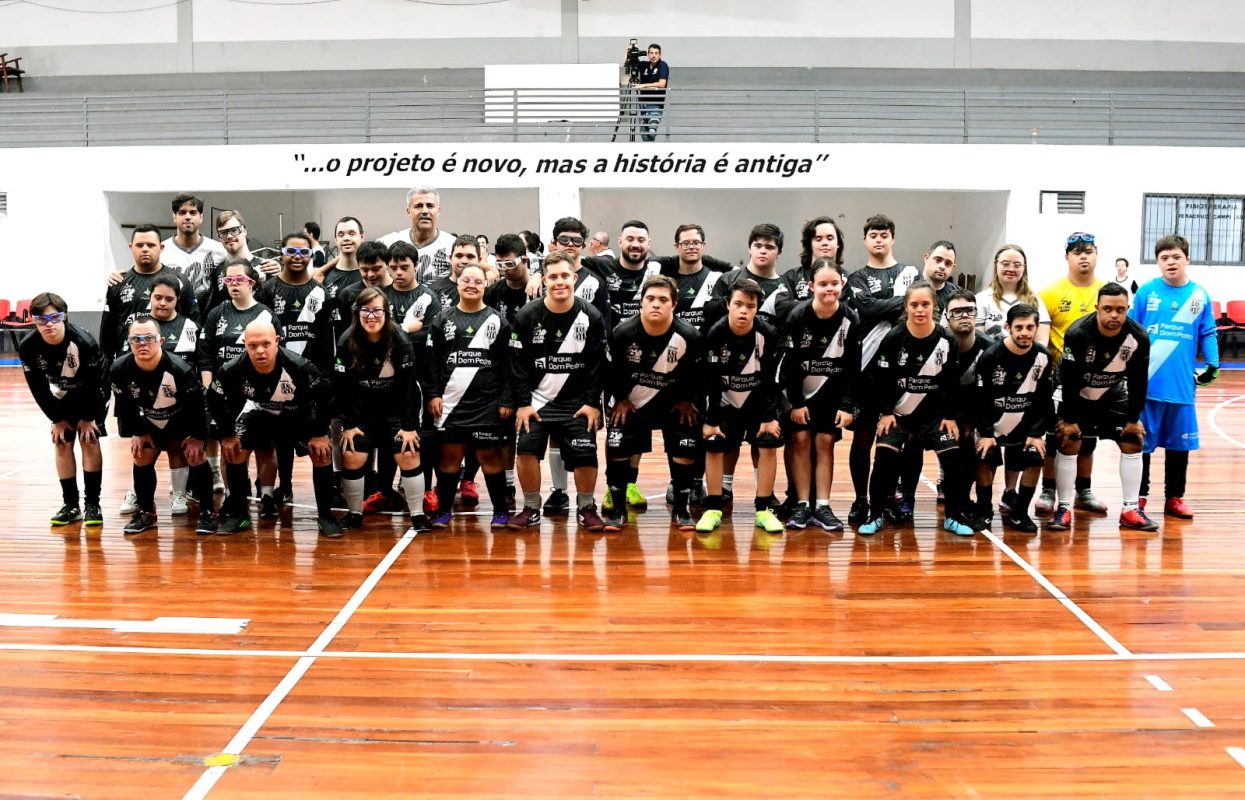 Foto colorida de atletas de futsal down da Ponte Preta S21 posando para a imagem. Eles usam uniforme e estão no centro da quadra.