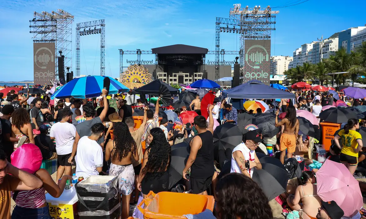 Foto colorida de várias pessoas na praia de Copabacana próximas ao palco do show de Lady Gaga no Rio de Janeiro.