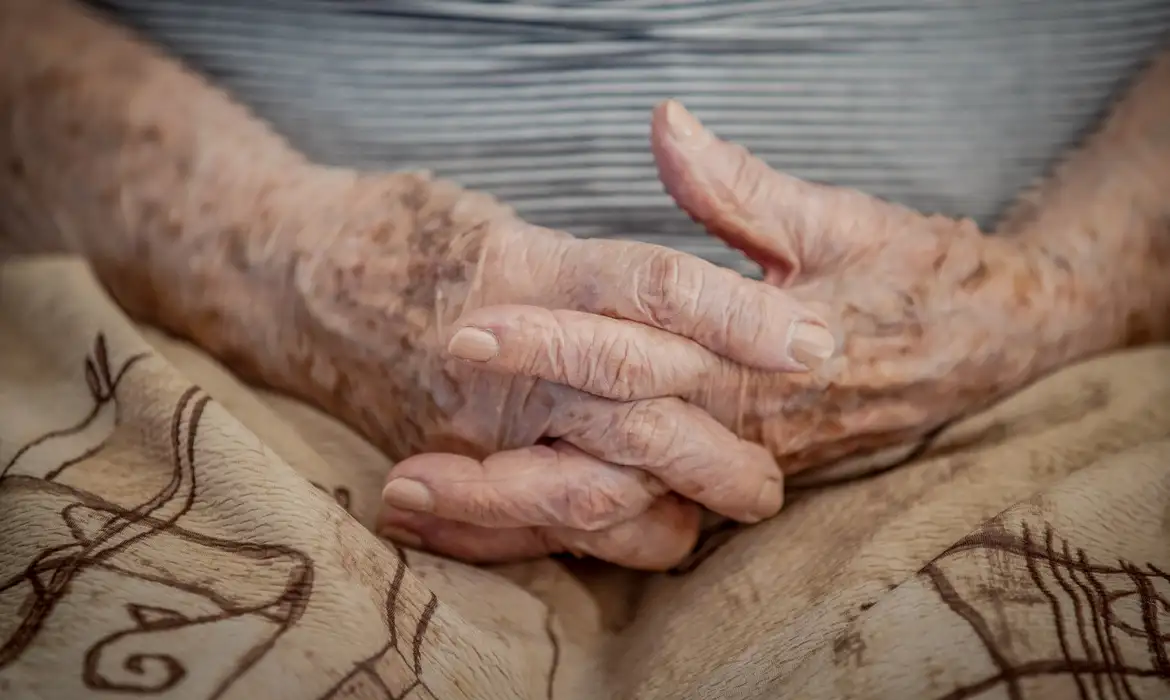 Foto colorida de close nas mãos de uma pessoa idosa