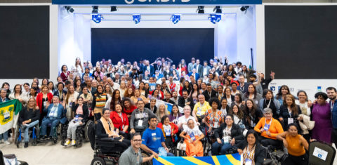 Foto colorida de um dos encontros da 5ª Conferência Nacional dos Direitos das Pessoas com Deficiência. Na imagem, aparecem diversas pessoas com deficiência reunidas na frente do palco, em Brasília (DF)