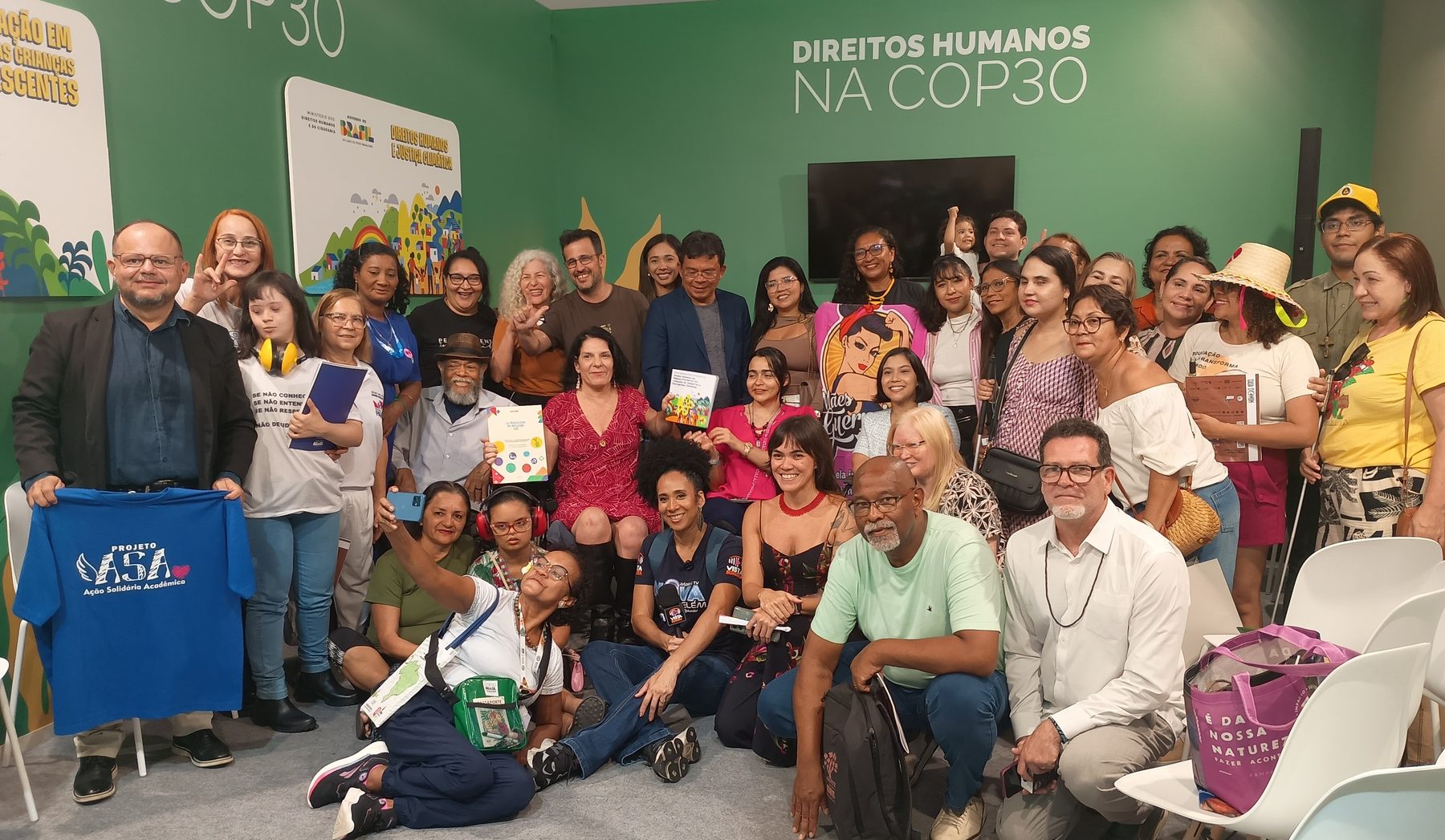 Foto colorida de pessoas que participaram da roda de conversa: “Emergência climática e resgate da dignidade". Elas posam para a foto no estande do Direitos Humanos na COP30