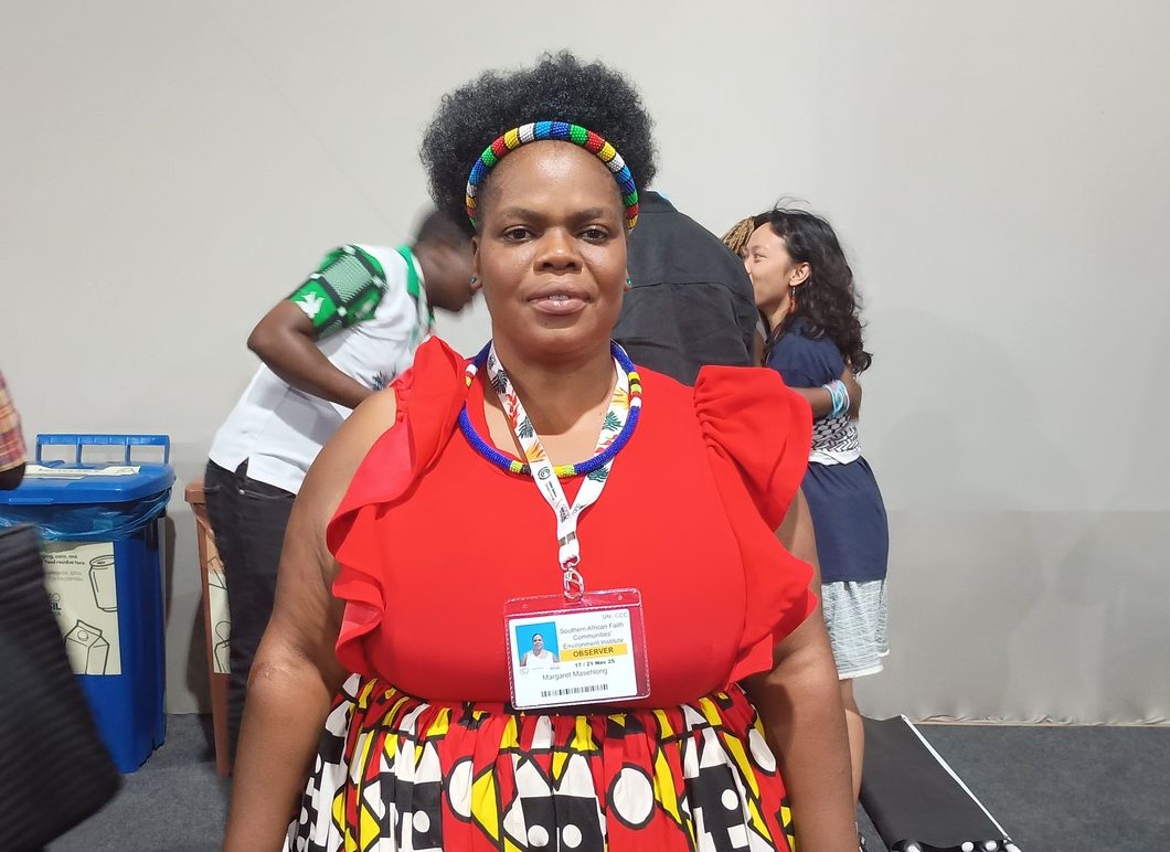 Foto colorida de Margaret Masehlog. Ela é uma mulher preta, com cabelo crespo curto. Ela usa uma blusa vermelha e uma saia colorida