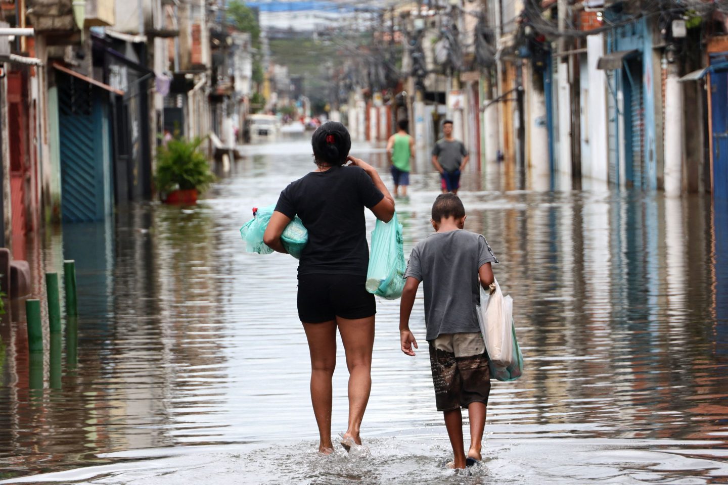 Foto colorida de pessoas andando em meio a rua alagada na zona leste de São Paulo após enchente. Situação revela relação entre clima e saúde