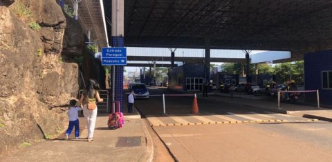Foto colorida que mostra mulher migrante ao lado de filho na entrada da fronteira entre Brasil e Paraguai