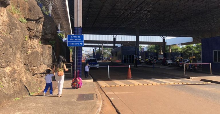 Foto colorida que mostra mulher migrante ao lado de filho na entrada da fronteira entre Brasil e Paraguai