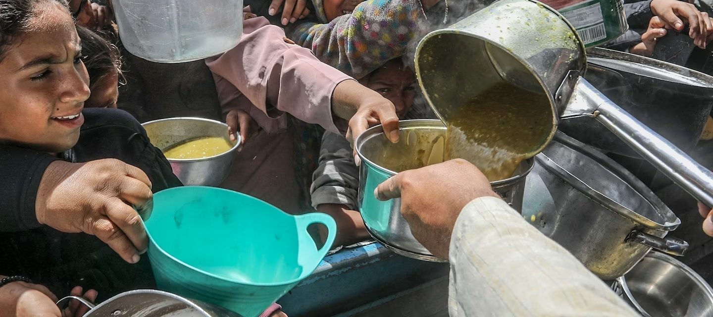 Foto colorida de pessoas com panelas, durante distribuição de alimentos na Faixa de Gaza em maio de 2025; insegurança alimentar cresce pelo mundo