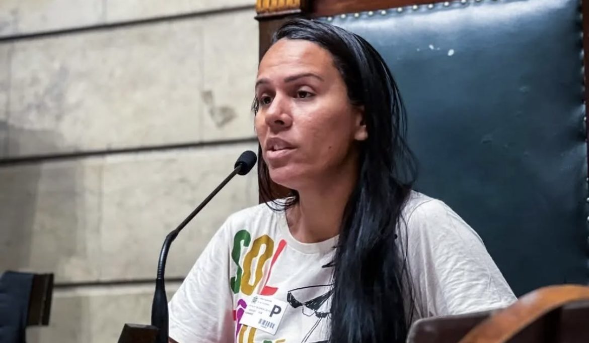 Foto colorida de Rafael França sentada em cadeira na Alerj. Ela é uma mulher negra, com cabelo liso preto longo e usa uma camisa branca