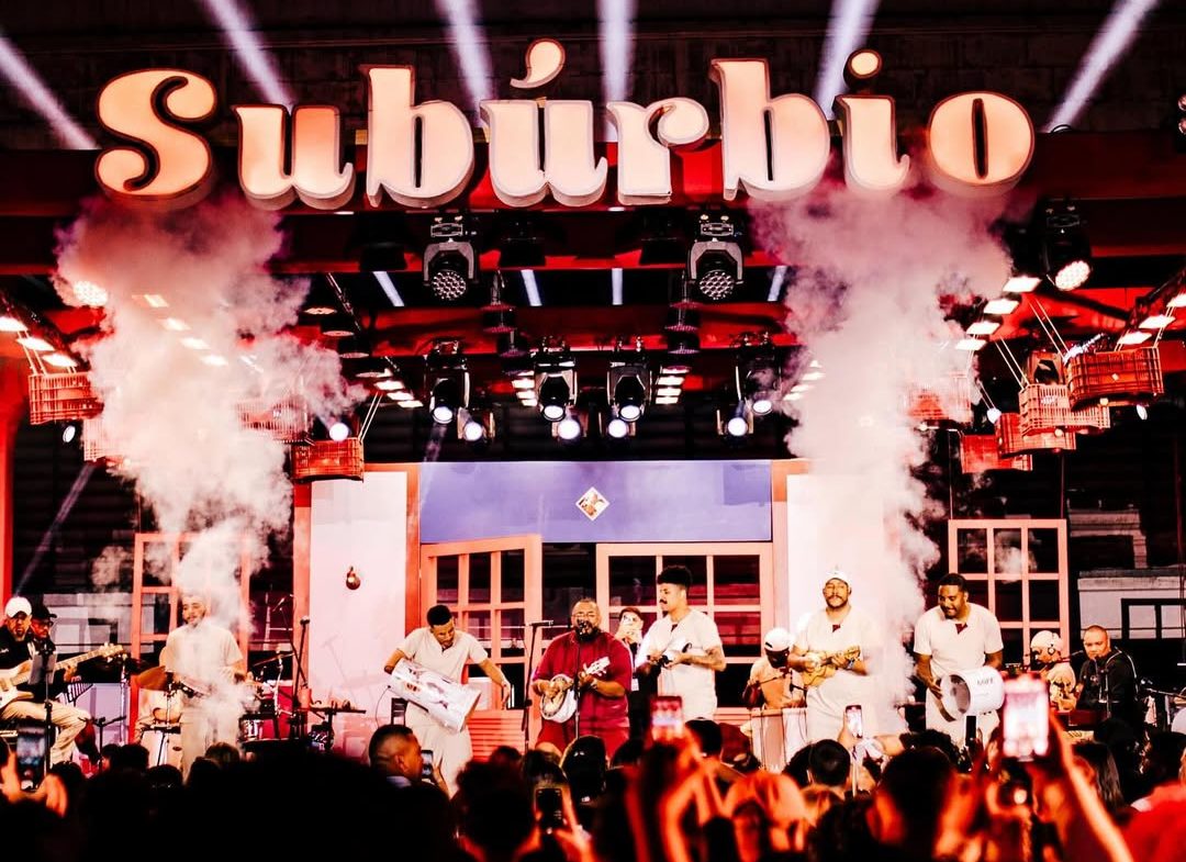 Foto colorida de palco do subúrbio, com Tiee e outros artistas no palco. Iniciativa envolve samba, solidariedade e valoriza modo de vida suburbano