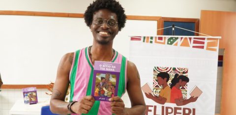 Foto colorida de Anderson Shon, homem preto com cabelo curto afro e segurando o livro Sitio da Tia Naná
