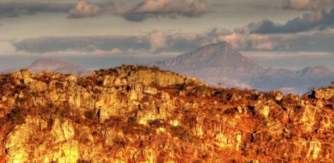 Foto colorida de rochas da Serra do Espinhaço, em Diamantina, Minas Gerais. Na imagem, é possível ver as montanhas sob uma luz amarelada.