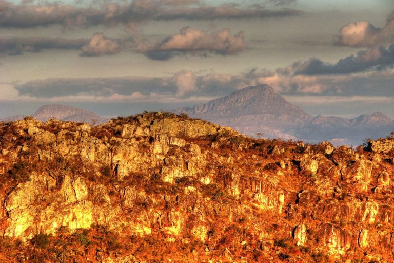 Foto colorida de rochas da Serra do Espinhaço, em Diamantina, Minas Gerais. Na imagem, é possível ver as montanhas sob uma luz amarelada.