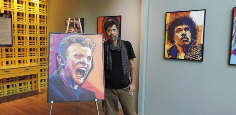 Foto colorida de Claudio Duarte ao lado de quadro com caricatura