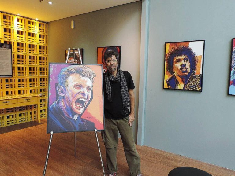 Foto colorida de Claudio Duarte ao lado de quadro com caricatura