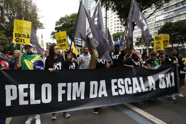 Foto colorida com manifestantes durante o grito dos excluídos no Rio de Janeiro. Eles seguram uma faixa preta com a frase, em branco: "Pelo fim da escala 6x1"