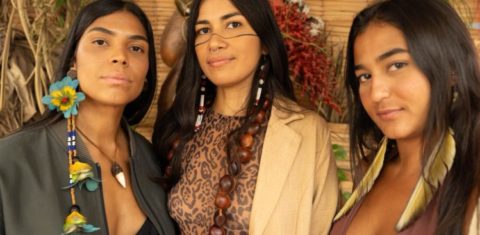 Foto colorida de Maiara Astarde, Vicka Tupi e Karol Kaysá. Criadoras do Sementes Urbanas, as três são mulheres indígenas e aparecem uma ao lado da outra, vestidas com adereços que remetem à sua cultura