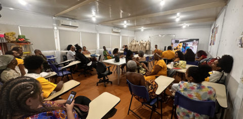 Foto colorida que mostra uma sala de aula do IFRJ, com várias pessoas negras e usando roupas tradicionais afro-brasileiras, coloridas