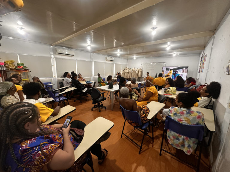 Foto colorida que mostra uma sala de aula do IFRJ, com várias pessoas negras e usando roupas tradicionais afro-brasileiras, coloridas