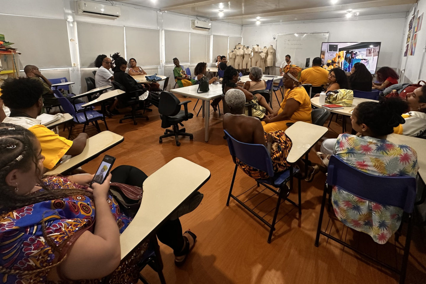 Foto colorida que mostra uma sala de aula do IFRJ, com várias pessoas negras e usando roupas tradicionais afro-brasileiras, coloridas